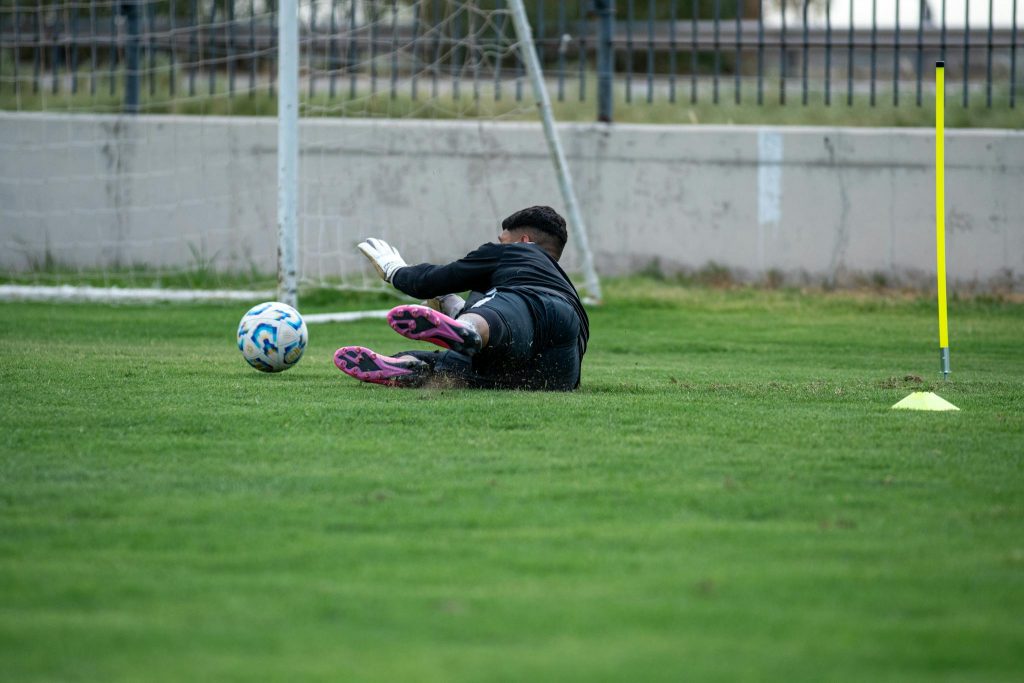 A soccer goalkeeper dives to save the ball during practice on a grassy field.